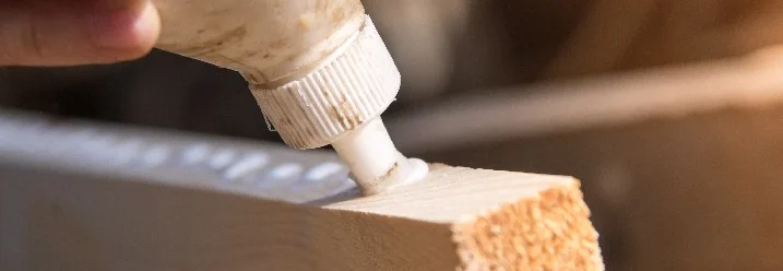 Person trägt Klebstoff auf Holz auf